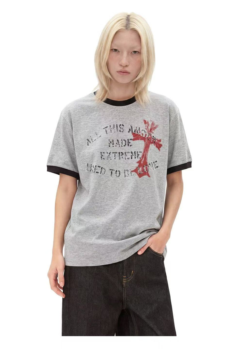 Model wearing a gray ringer T-shirt with distressed cross graphic and black trim, styled with dark jeans
