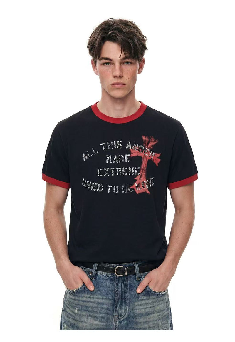Black ringer T-shirt with red trim and distressed cross graphic, worn with faded blue jeans on a male model