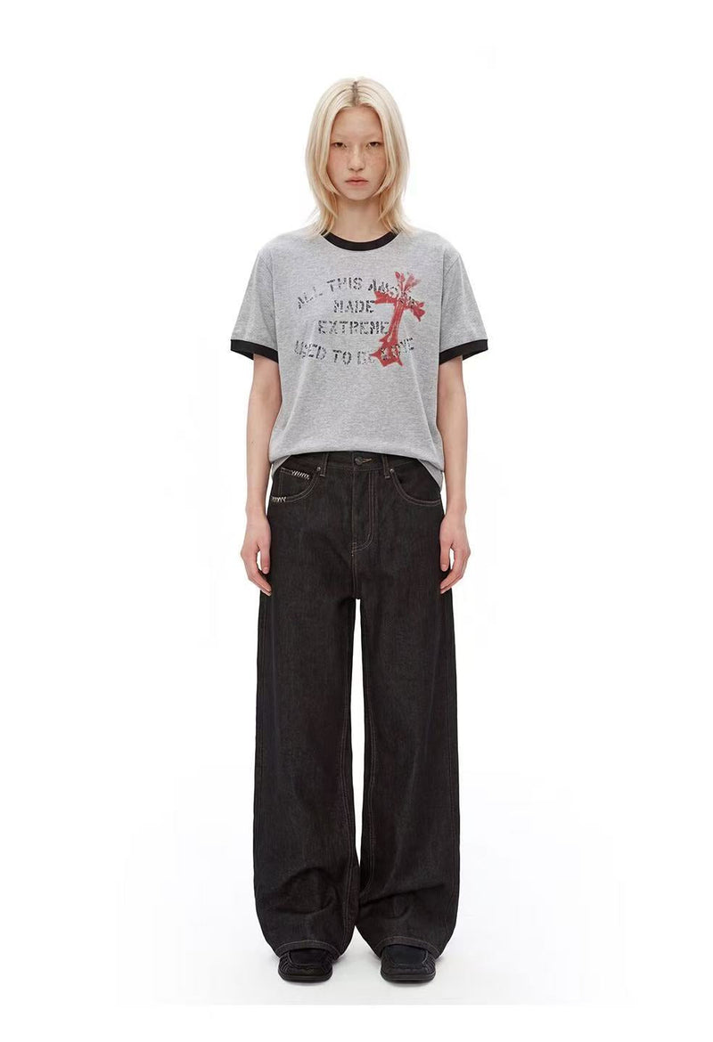 Model wearing a gray ringer T-shirt with distressed cross graphic and loose black wide-leg jeans on white background