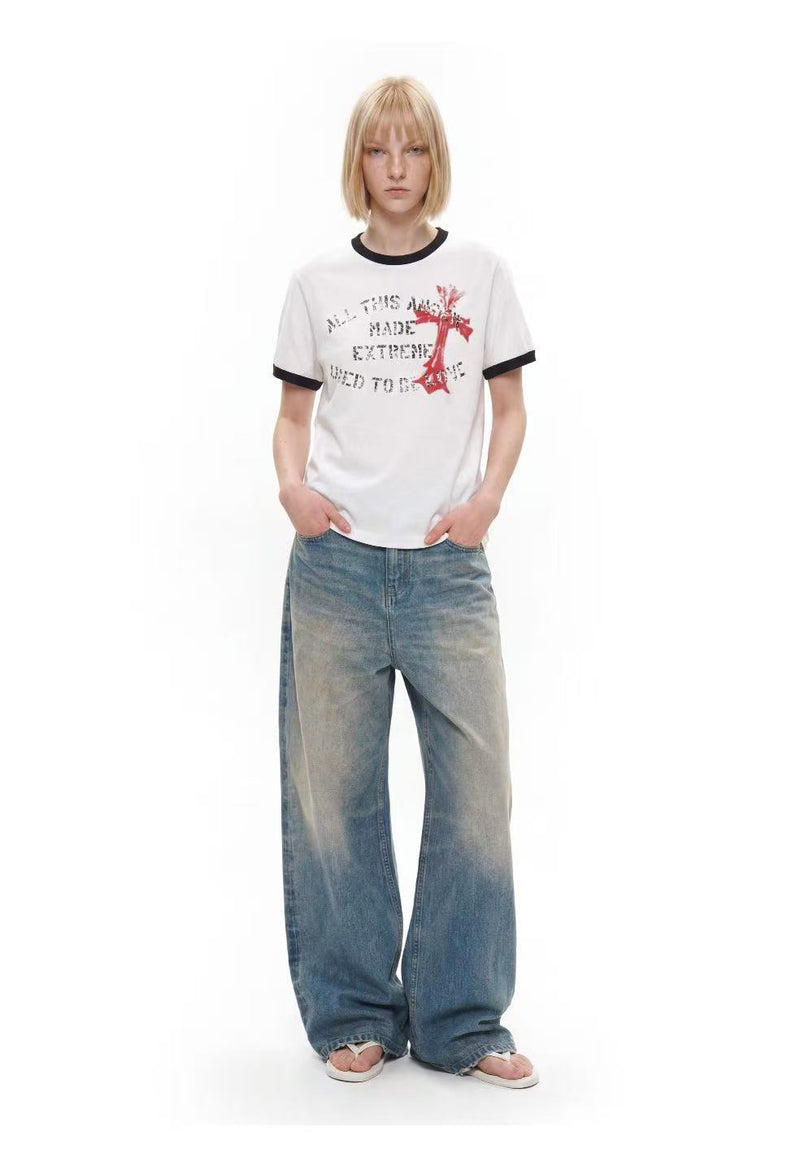 White ringer T-shirt with black trim, distressed cross graphic print, styled with loose faded jeans and sandals on model