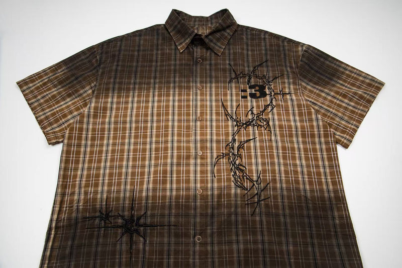 Brown plaid short-sleeve button-up shirt with black graphic print and vintage streetwear style