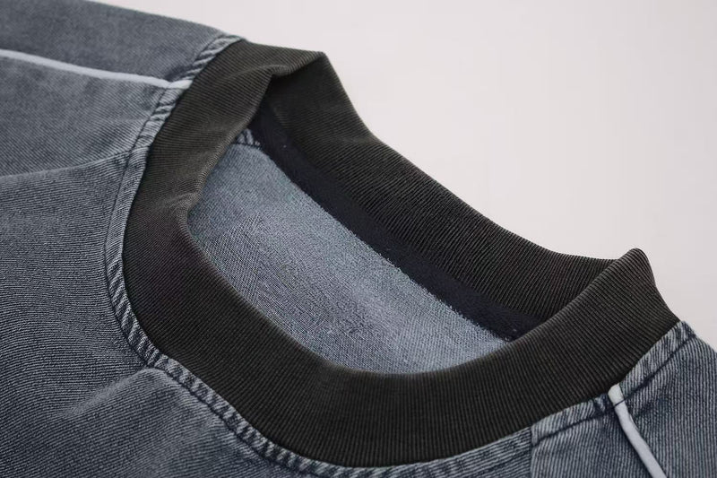 Close-up of a vintage washed distressed graphic T-shirt with black ribbed collar and faded blue denim-like texture