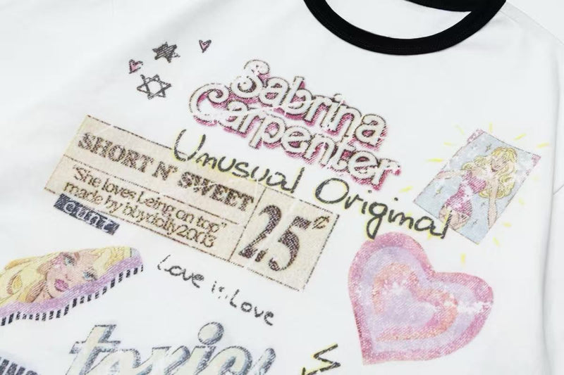White ringer tee with black collar and colorful retro pop graphic collage featuring hearts, stars, and playful text print