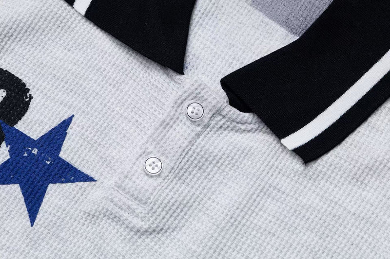 Close-up of a textured white polo tee with black striped collar, button placket, and blue embroidered star graphic