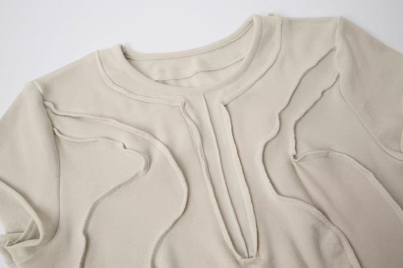 Beige cotton tee with raw seam sculpted panel detailing and a crew neck, shown laid flat on a clean background
