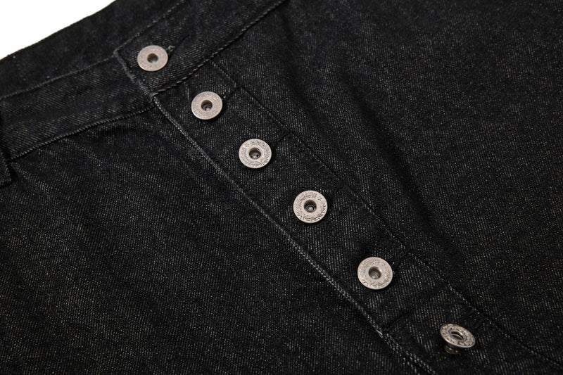 Close-up of black denim fabric and silver-tone buttons on the asymmetrical front placket