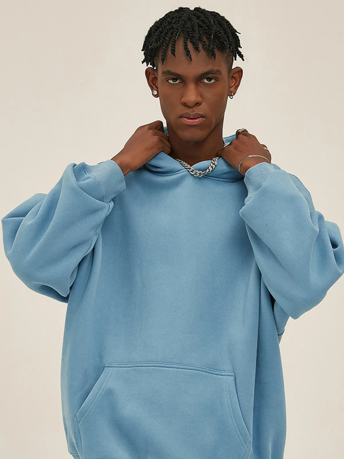 A person in the Custom Anime Character Sky Blue Hoodie—Personalized 350GSM 100% Cotton Pullover stands against a beige background, holding the collar to showcase its cozy and stylish appeal.