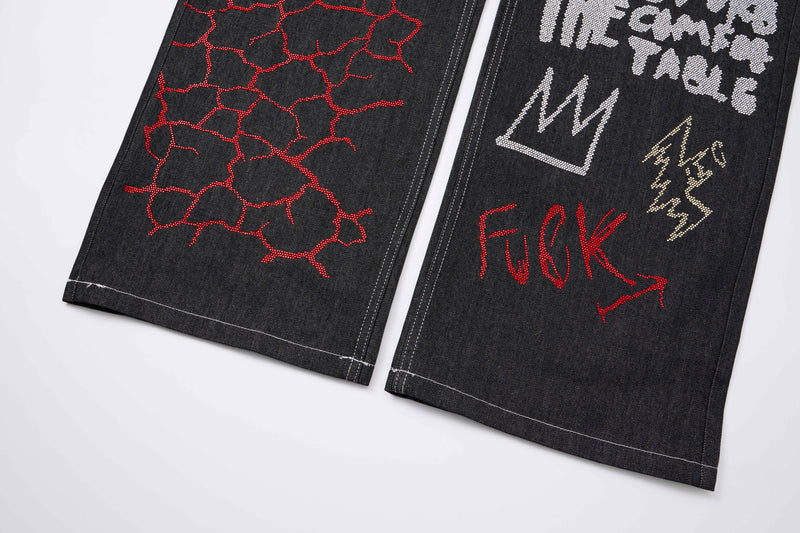 Lower leg view of black jeans with red crackle graphic and rhinestone text details
