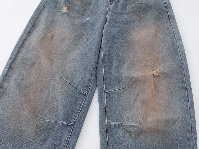 Front thigh detail of faded blue jeans with ripped distressing and patch marks