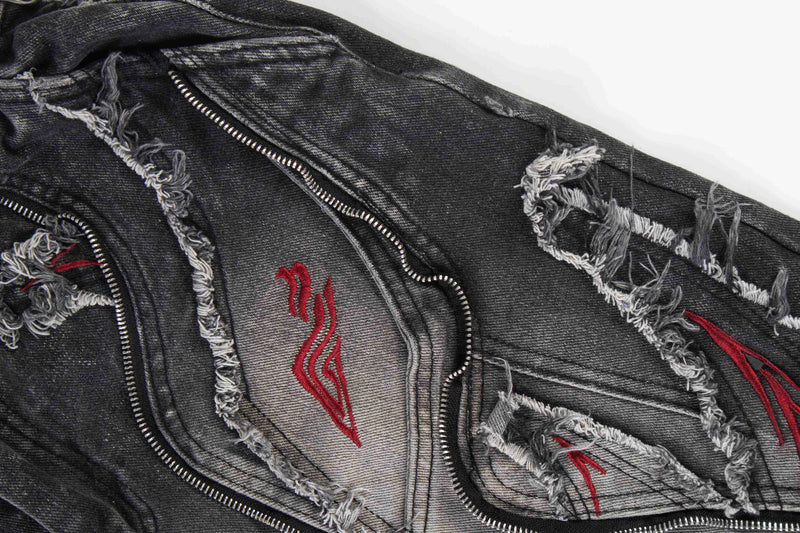 Close-up of front panel on black baggy jeans with zipper trim, frayed rips, and red embroidery