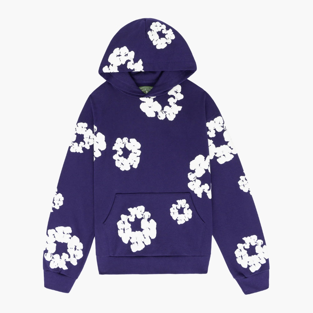 The Purple “Cotton Wreath” Denim Tears Hoodie is a streetwear pullover with a front pocket, featuring large white floral prints on purple fabric, inspired by the iconic Denim Tears style.