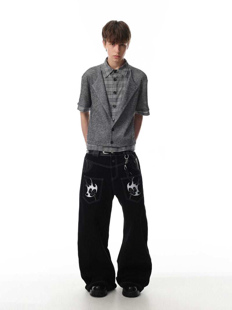 Model wearing a layered gray knit check shirt with short sleeves, plaid underlayer, and black wide-leg jeans with graphic pockets
