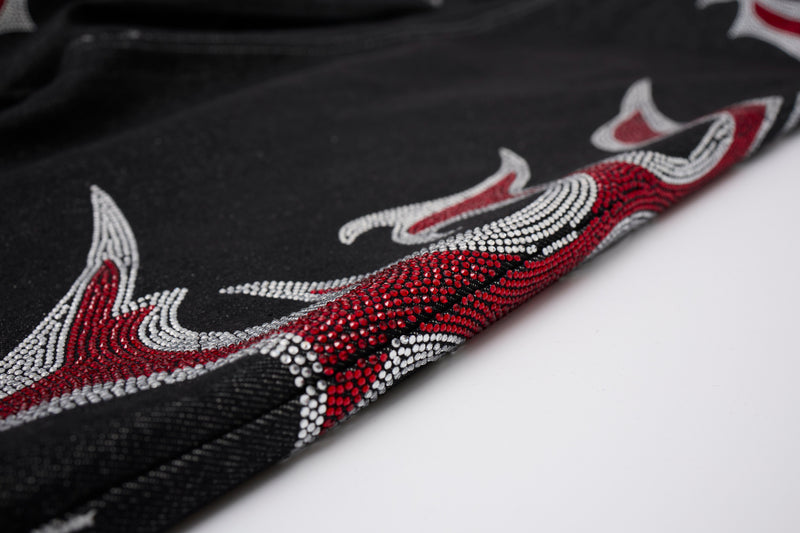 Close-up of lower leg hem on black denim pants with red and silver rhinestone flames
