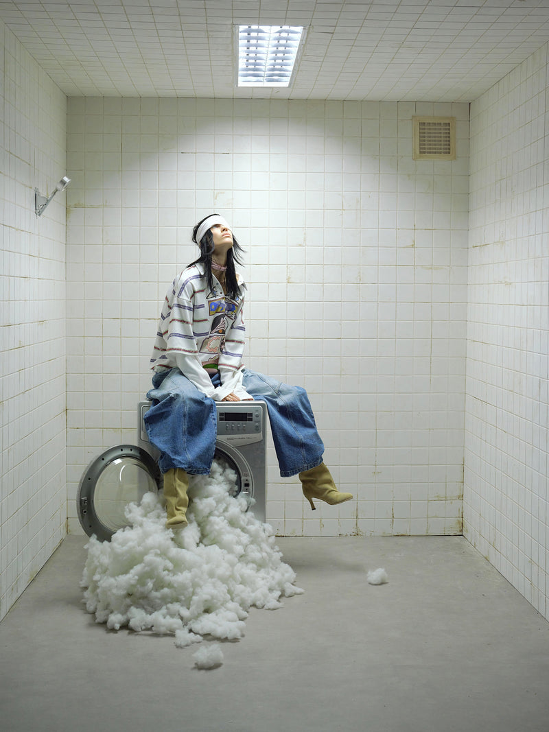 Model wearing white graphic long-sleeve polo shirt sitting on washing machine