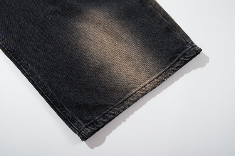 Close-up of wide-leg hem on black fade denim with frayed edge and faded tan wash