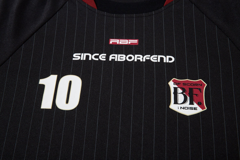 Close-up of black jersey front with number 10, chest logo, and red collar