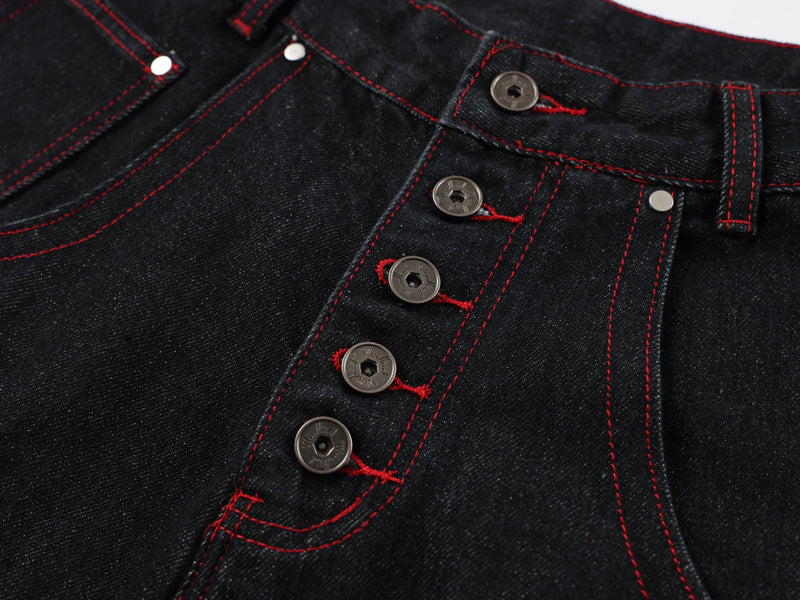 Close-up of button fly and front pocket on black denim pants with red topstitching