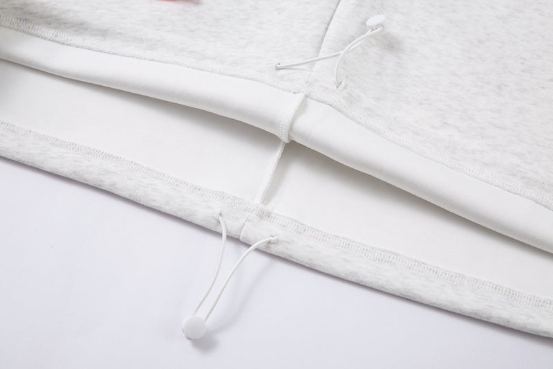 Close-up of the lower hem with white drawstring ends on a light gray hoodie