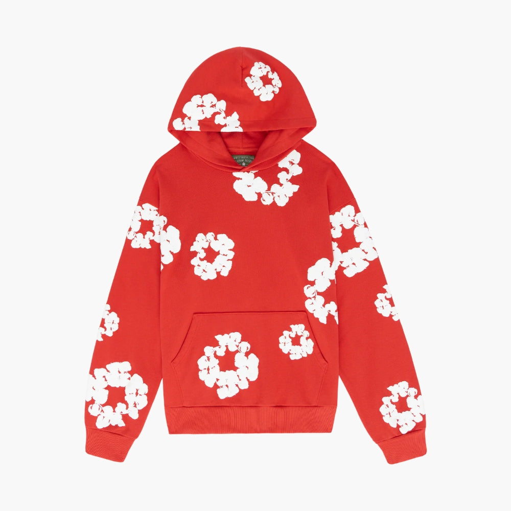 The Red “Cotton Wreath” Denim Tears Hoodie is a red streetwear pullover with white floral prints, kangaroo pocket, and cotton wreath-inspired design across the front, sleeves, and hood, shown laid flat on a plain white background.