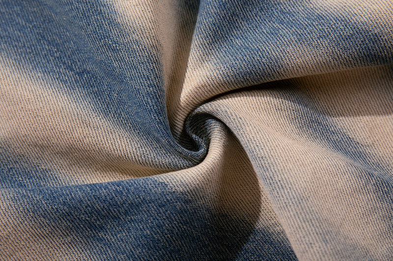 Close-up of denim fabric showing blue and cream spray-fade graffiti wash texture