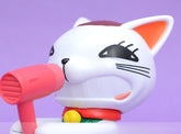 A close-up of the Dandadan Lucky Cat PVC Figure shows a kawaii white cartoon cat with big black eyes, orange-tipped ears, and a wide grin holding a pink microphone. Set against a purple backdrop, it&