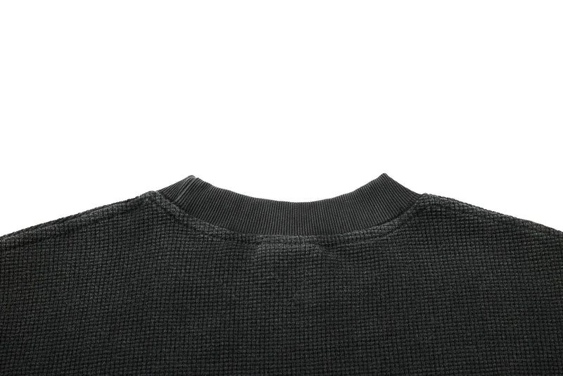 Close-up of a black waffle knit graphic T-shirt with a ribbed crew neck and textured vintage finish