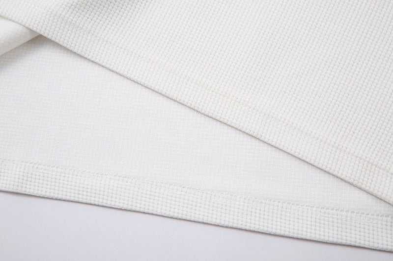 Close-up of white cuff and hem seams on textured waffle knit fabric