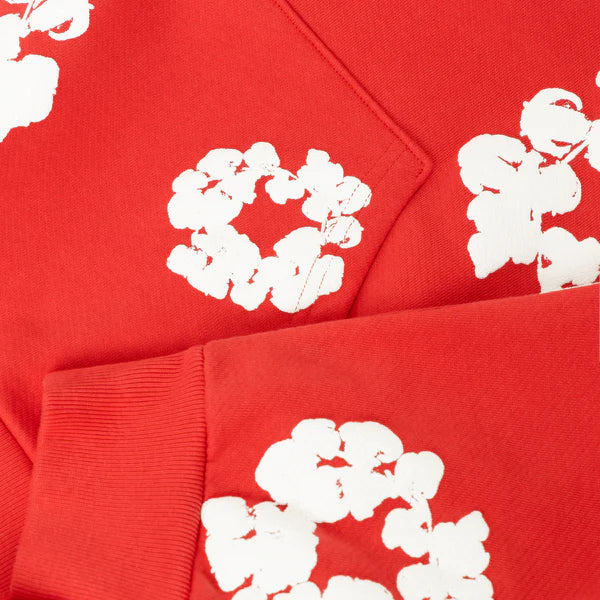 Close-up of the Red “Cotton Wreath” Denim Tears Hoodie, a streetwear pullover featuring bold white floral prints on red fabric with visible folded sleeve and stitching details.
