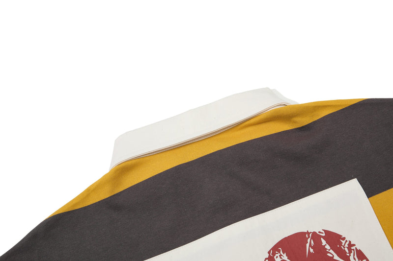 Close-up of a striped rugby polo in white, mustard yellow, and charcoal with a red graphic print on the chest