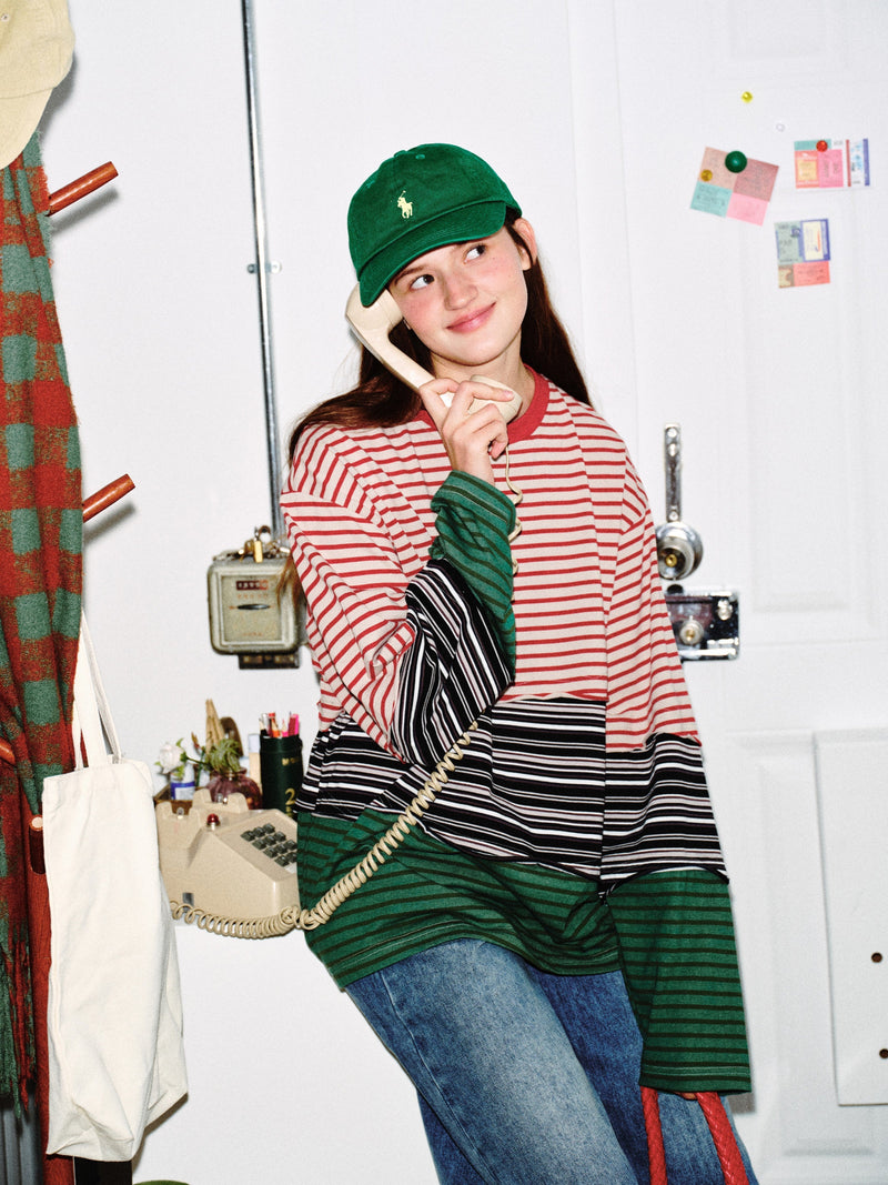 Model wearing color-block striped long sleeve tee with red, black, and green stripes, side view