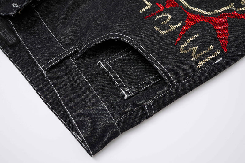 Close-up of black denim hem with contrast stitching and graffiti rhinestone detailing