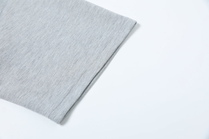 Close-up of a light gray oversized tee sleeve with asymmetric seam detail and textured streetwear fabric