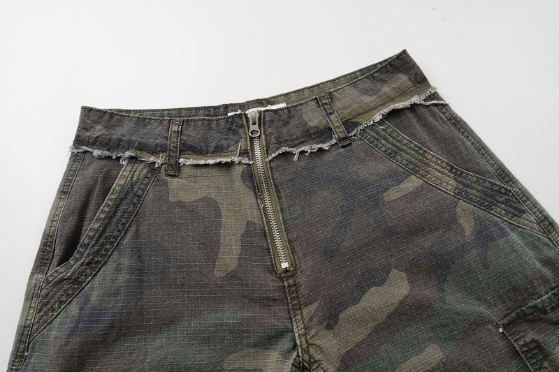 Front upper view of camouflage cargo shorts with zipper fly, belt loops, and raw waistband edge