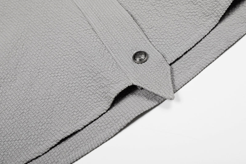 Close-up of a light gray textured cotton shirt with asymmetrical hem and decorative stand-collar button detail