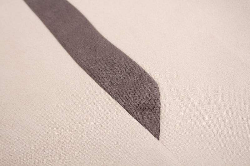 Close-up of a cream athletic T-shirt with a dark suede-textured diagonal panel detail