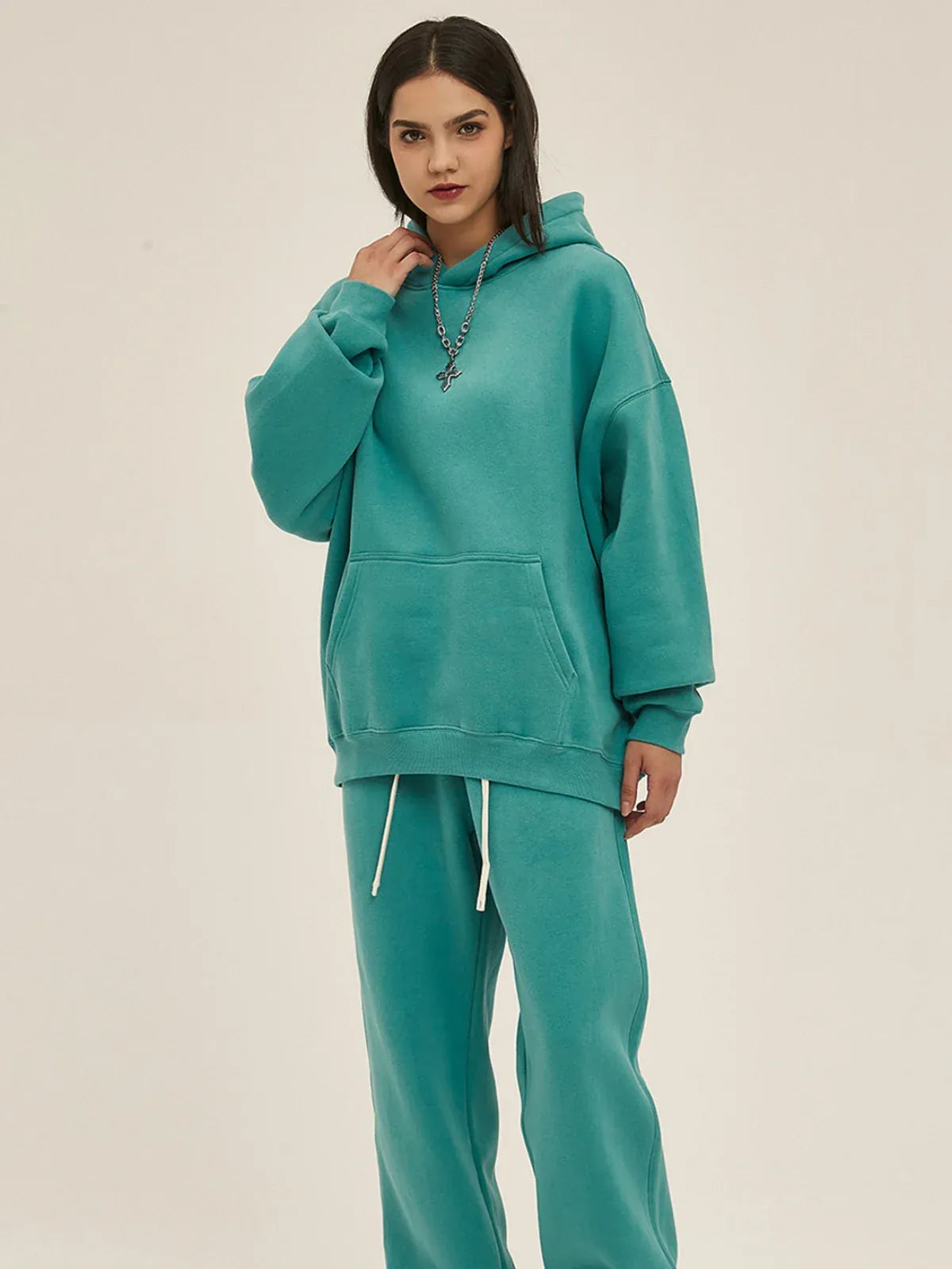 Person wearing a Custom Anime Character Dusty Teal Hoodie - Personalized 350GSM 100% Cotton Pullover, paired with matching sweatpants, stands against a plain beige background.