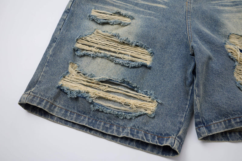 Close-up of distressed blue denim shorts leg with frayed holes and light fading
