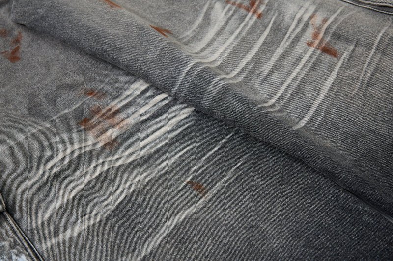 Close-up of gray denim fabric with white paint streaks and brown splatter
