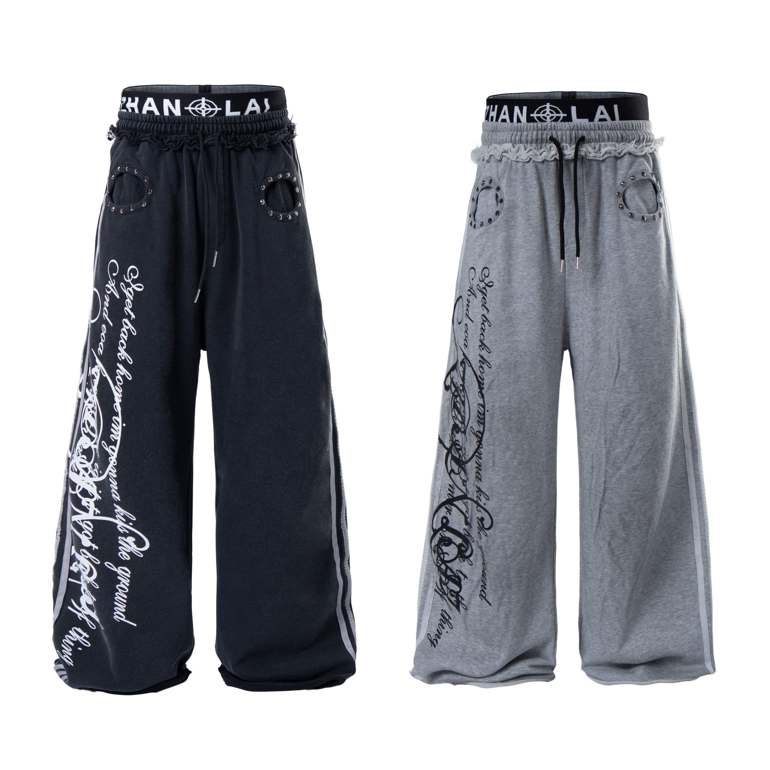 Front view of black and grey wide-leg sweatpants with cursive graffiti script print and rivet-accented pocket cutouts