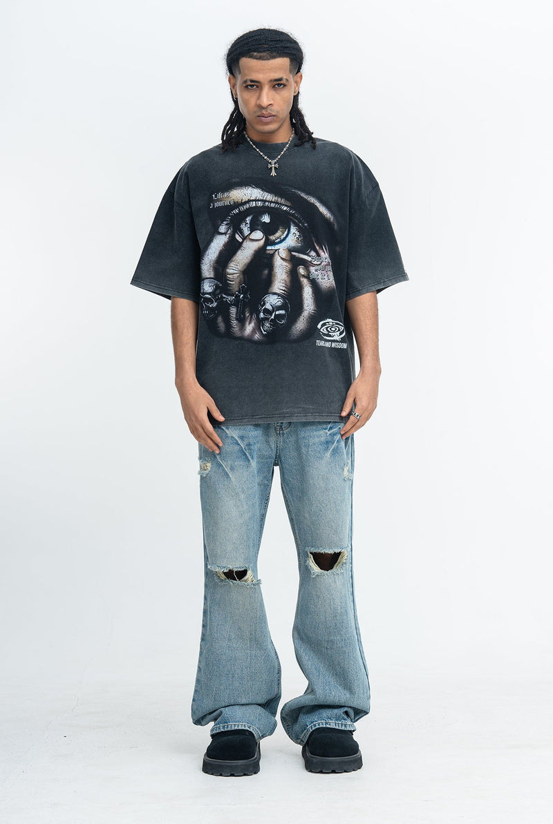 Oversized black graphic tee with eye print, worn with distressed light wash jeans and black shoes