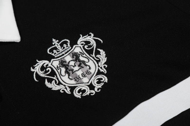 Black polo shirt with white striped trim and ornate embroidered crest detail on the chest