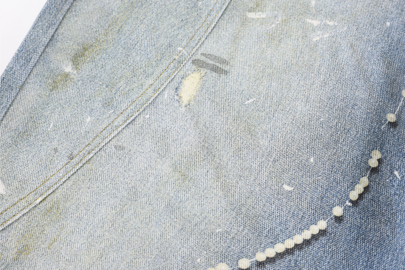Close-up of curved leg seam with distressed denim and bead trim along the side