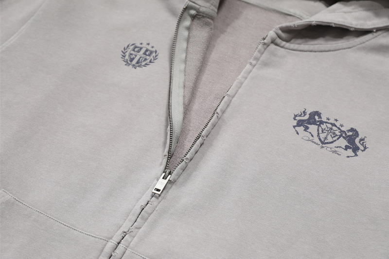 Close-up of light gray hoodie front with small crest print and larger graphic on chest