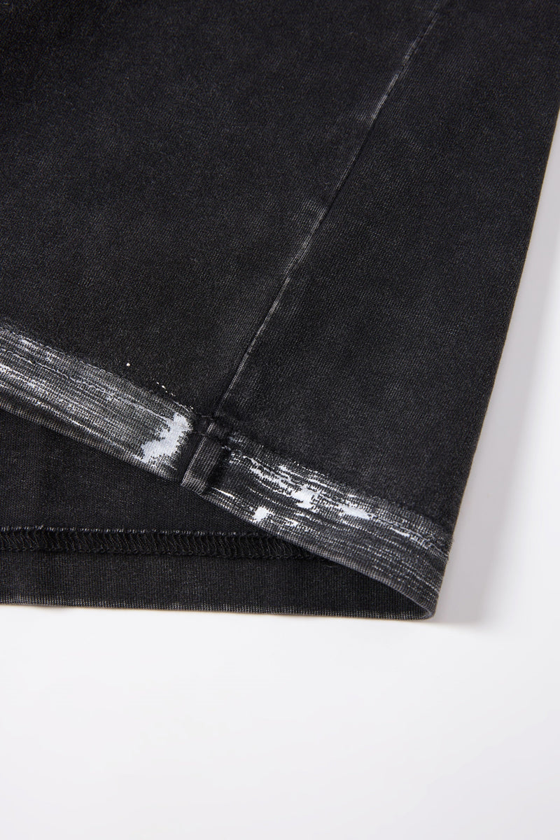 Close-up of a washed black boxy cotton T-shirt hem with faded raw-edge stitching and streetwear detailing