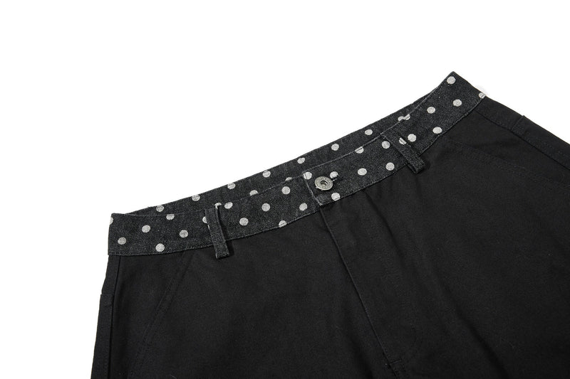Close-up of black denim waistband with white polka dots, belt loops, and button closure
