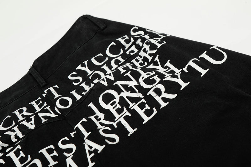 Close-up of overlapping white typography print on black pants at the back waist