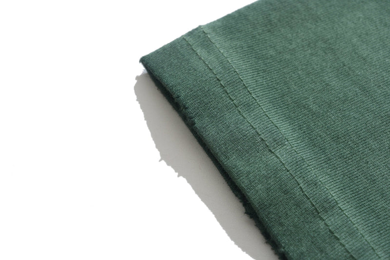 Close-up of a green vintage wash graphic tee sleeve with visible hem stitching on a white background