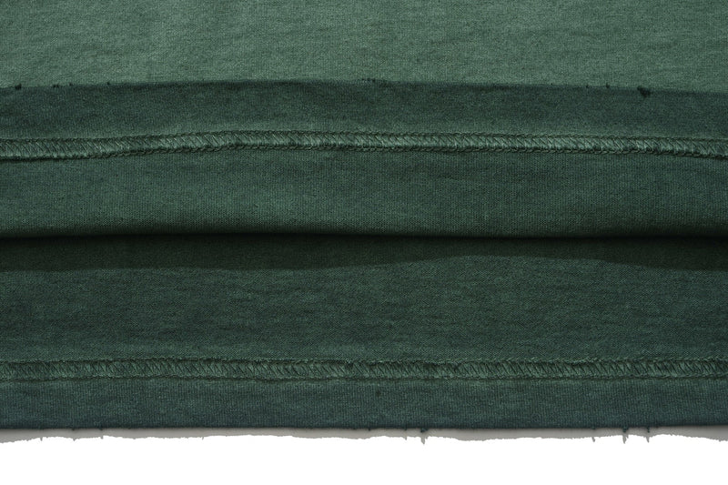 Close-up of a dark green vintage wash graphic tee with layered seam details and distressed hem