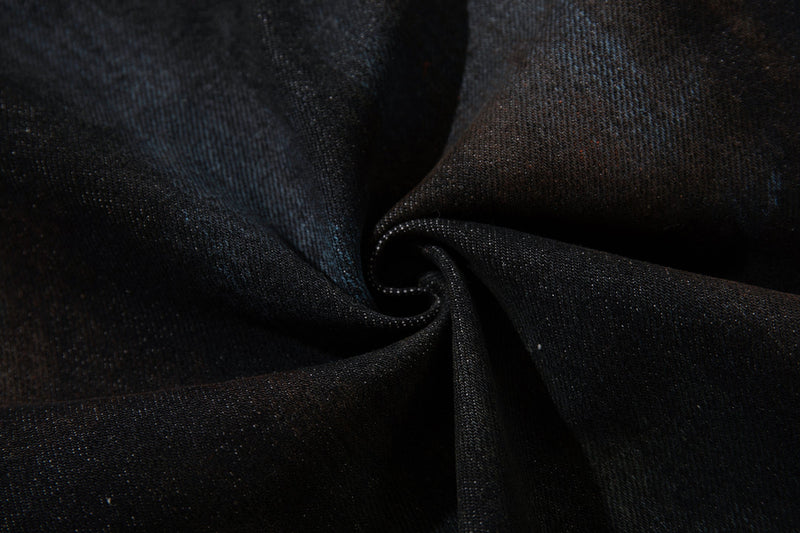 Close-up of dark denim fabric with a twisted fold and painted wash texture