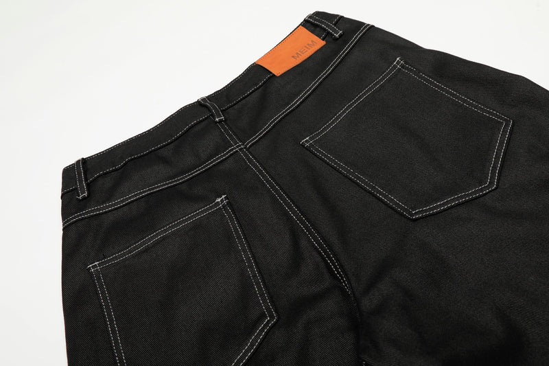 Close-up of the back waistband and pocket on black denim pants with orange label patch